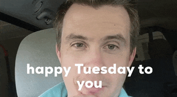 Video gif. Man sits in his car and records himself giving us a positive message, cheerfully saying, "happy Tuesday to you," which appears as text.
