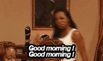 Reality TV gif. On Flavor of Love, while other contestants sit at a dinner table, Tiffany Pollard walks down smiling, pointing and saying "good morning! good morning!" which appears as text.