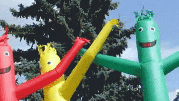 Video gif. Red, yellow, blue, and green air dancers flap wildly in the wind. 