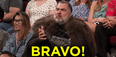 Video gif. A bearded man sits in an audience and wears Viking battle clothes. He claps enthusiastically along with the audience. Text, "Bravo!"