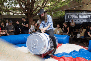 Ad gif. A man riding a mechanical bull in the shape of a Young Henry's can is whipping his arm over his head as he balances himself.