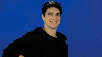 Celebrity gif. Brendon Urie smiles and slowly lifts up his black shirt, revealing an image of a cursor flashing the middle finger on his chest.