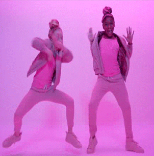 Music video gif. From Charli XCX's "After the After Party," two dancers with topknot buns, wearing all-pink outfits and cast in pink lighting, dancing wildly, stepping and waving their arms.