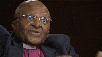 Video gif. Archbishop Desmond Tutu flashes excited eyes and seems to say "Oh" during an interview.