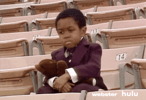TV gif. Emmanuel Lewis as Webster, dressed in a suit and sitting alone on a stadium seat, holds a teddy bear on his lap, blinks and then leans his elbow on his knee, resting his chin on his fist, looking wistfully to the side.