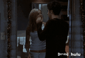 TV gif. Zach Braff as JD in Scrubs pushes Sarah Chalke as Elliot's hair behind her ears, draws her face to his, and they kiss passionately.