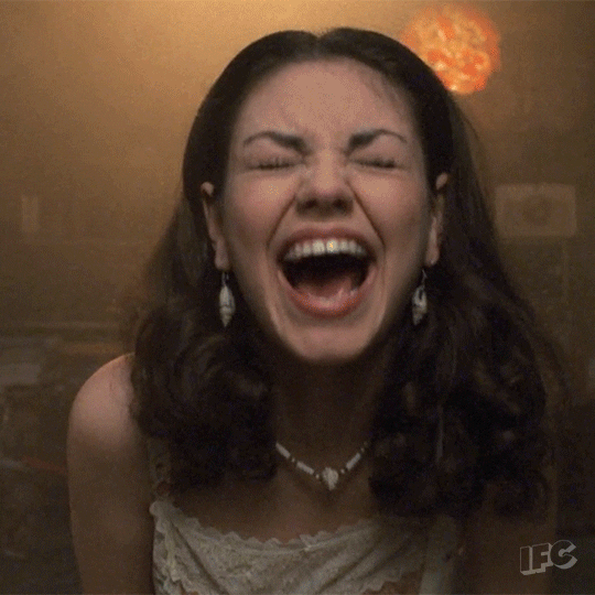 TV gif. Mila Kunis as Jackie in That Seventies Show throws herself forward and backward as she laughs hysterically. 