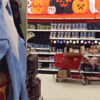 Video gif. Child in a hot dog costume appears in a Target aisle and strikes a pose, hand on his hip, before strutting towards us like a model on a runway.