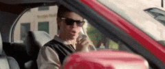 Movie gif. Ansel Elgort as Baby in Baby Driver is singing in his car with wired earbuds in, using a water bottle like a microphone.
