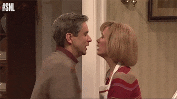 SNL gif. Kristin Wiig and Fred Armisen dress like stereotypical wife and husband. They both twirl next to each other and then they kiss.