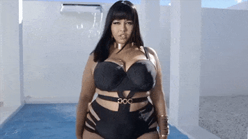 Video gif. A curvy fashion model is wearing a black bodysuit that has cut outs at the side and the hips. She smizes at us before putting her hands at her hips.  