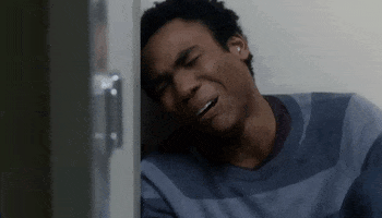 TV gif. Donald Glover as Troy in Community leans against a wall as he cries hysterically. 