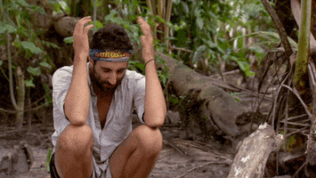 Reality TV gif. Contestant on Australian Survivor squats on the dirt in the middle of the woods and smacks the top of his head with both hands, as if he's trying to get himself to think more clearly.