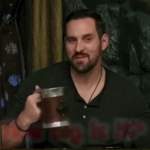 Video gif. In a clip from Critical Role, Travis Willingham smirks as he tries to catch us in a lie. Text, "How big is it? If you've seen it." Then, he drinks from a beer stein.