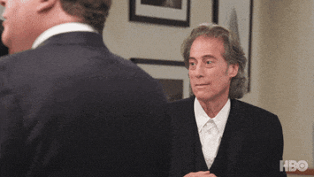 TV gif. Richard Lewis on Curb Your Enthusiasm looks resigned, shrugs, and smiles