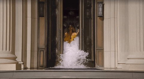 Beonce wearing flowing yellow gown opening double doors as water rushes past her.