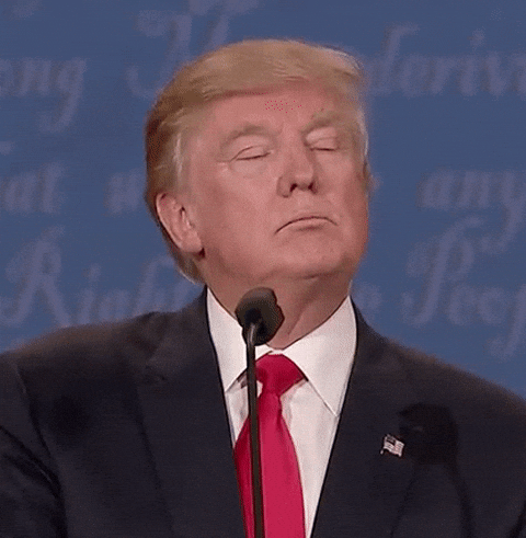 Video gif. At a presidential debate, Donald Trump stands behind a podium, narrows his eyes and takes a sip of water from a clear glass.