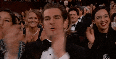 Celebrity gif. Andrew Garfield seated in the audience at the Oscars. His mouth opens wide like he's cheering as his hands clap in front of him energetically. 