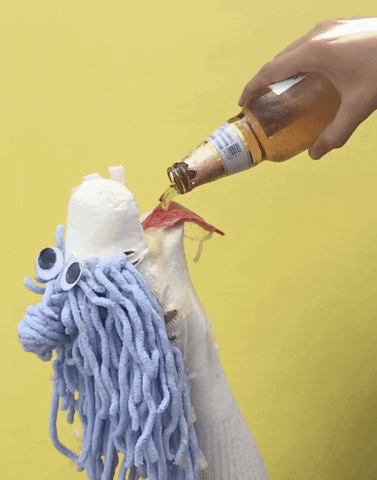 Video gif. White sock puppet with periwinkle hair tilts its head back and opens its mouth wide as a bottle of beer is poured in and splashes out.