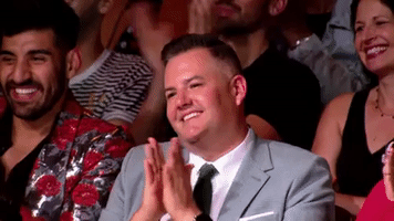 Reality TV gif. Ross Matthews in the audience watching the grand finale of RuPaul's Drag Race gives a small smile and small clap as he sees the winner.