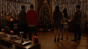 TV gif. Five cast members from New Girl stand facing a brilliantly lit Christmas tree. The lights begin to flicker before the apartment goes dark.