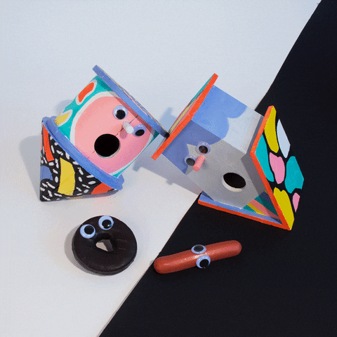 Stop motion gif. Two birdhouses with googly eyes are gaping at a sausage that enters into a donut hole.