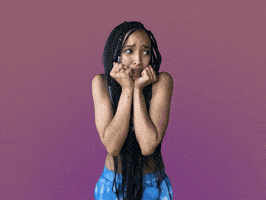 Celebrity gif. Tinashe has both her fists on her chin and she looks side to side, scared and nervous. 