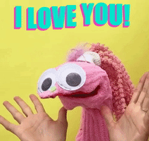 Video gif. A puppet made out of a pink wool sock with a scrunchy and a pink ponytail smiles with giant googly eyes. It's human hands open with excitement before she puts them on her face, as she says, "I love you!"