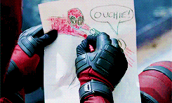 Movie gif. We are peering over the shoulder of Wade Wilson, aka Deadpool, working on a kidlike crayon drawing of himself killing someone on a piece of paper; the victim says, "Ouchie!"