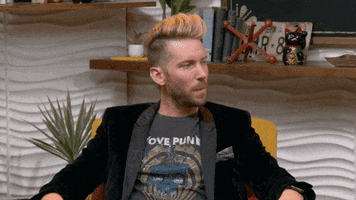 Video gif. Troy Baker sits in an chair and flips his hands in a shrug as he turns his head and says, "It's Wednesday."