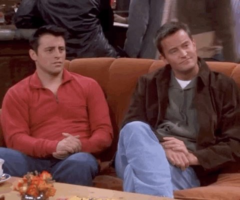 Joey og Chandler fra FRIENDS sitter i en sofa, ser på hverandre, og ser så bort på et felles punkt mens de applauderer anerkjennende