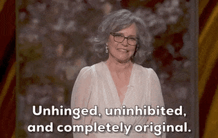 Oscars 2024 GIF. Sally Field wears a flowy white dress, dangling silver earrings and black glasses. She directs her gaze at us and says with spirit, "Unhinged, uninhibited, and completely original."
