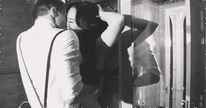 GIF em preto e branco, de homem e mulher de sutiã se beijando enquanto ela está encostada na parede 