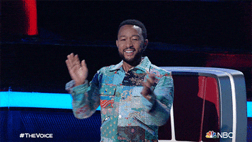Reality TV gif. John Legend smiles and claps vigorously as a coach on The Voice.