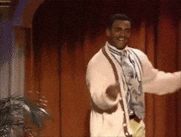 TV gif. Alfonso Ribeiro as Carlton on The Fresh Prince of Bel Air. He's wearing a cardigan and looks uttery jovial as he swings his arms around and performs the Carlton dance on stage.