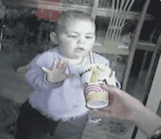 Video gif. A hand holds a drink with a straw to a window outside as a baby inside tries to drink it. 