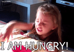 Video gif. A little girl in a black t-shirt throws a tantrum, pounding on a bed and yelling angrily. Text, "I am hungry!"