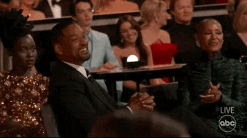 Celebrity gif. Will Smith bursts out laughing and clapping and looks at Jada Pinkett Smith, who laughs along with him, at the 2022 Oscars.