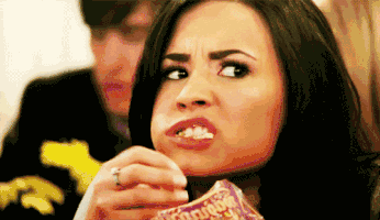 Celebrity gif. Demi Lovato appears captivated by something, stuffing her mouth with popcorn.