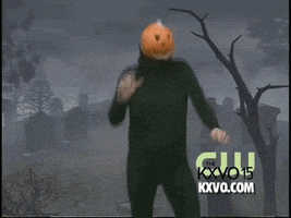 TV gif. Man in a black leotard wearing a jack-o-lantern mask swinging his hips in front of a green screen graveyard. 