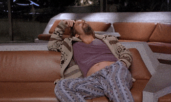Movie gif. Jeff Bridges as The Dude from The Big Lebowski does not abide, alone and bored, rocking his leg back and forth. He leans back against a couch, scratching his head.