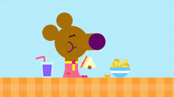 Cartoon gif. Norrie from Hey Duggee sits on a table, next to a cup of grape juice and a bowl of cheese curls. The mouse holds a jelly sandwich in her little hand and happily chews.