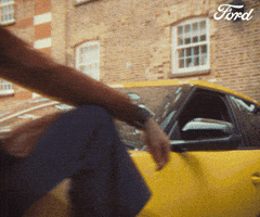 Sponsored gif. Man stands with one leg bent against the front tire of a yellow car. He tips his sunglasses to the end of his nose, looks over the frames, and then nods his head. Text reads, “You got this!”