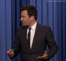 Tonight Show gif. Jimmy turns up his hands in mildly frustrated confusion. Text, "What."