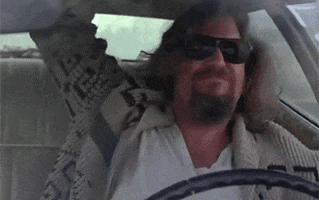 Movie gif. Jeff Bridges as The Dude in the Big Lebowski wears sunglasses and taps on the ceiling of a car as he rocks out behind the wheel.