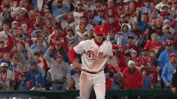 Sports gif. Slow motion video of Rhys Hoskins of the Philadelphia Phillies punching his fists in towards his body and yelling in intense celebration as the crowd goes wild behind him. 