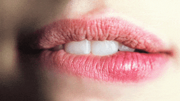 Video gif. Close-up on a woman's pink lips as she bites the side of her bottom lip in a sexy, sultry manner. 