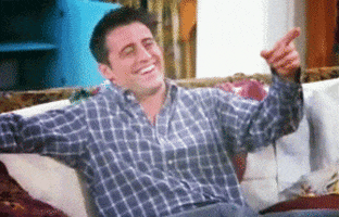 Friends gif. Matt LeBlanc as Joey points throws his head back in laughter as he sits on the sofa. 