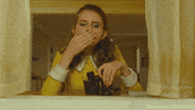 Movie gif. Kara Hayward as Suzy in Moonrise Kingdom next to a window, holding binoculars and glancing down at us with seriousness as she blows a kiss.