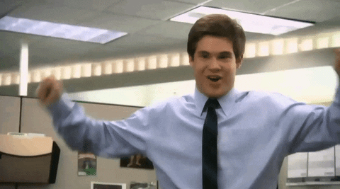 TV gif. Adam Devine as Adam Demamp on Workaholics stands in an office cubicle. He lifts his fists up in celebration and smiles excitedly.
